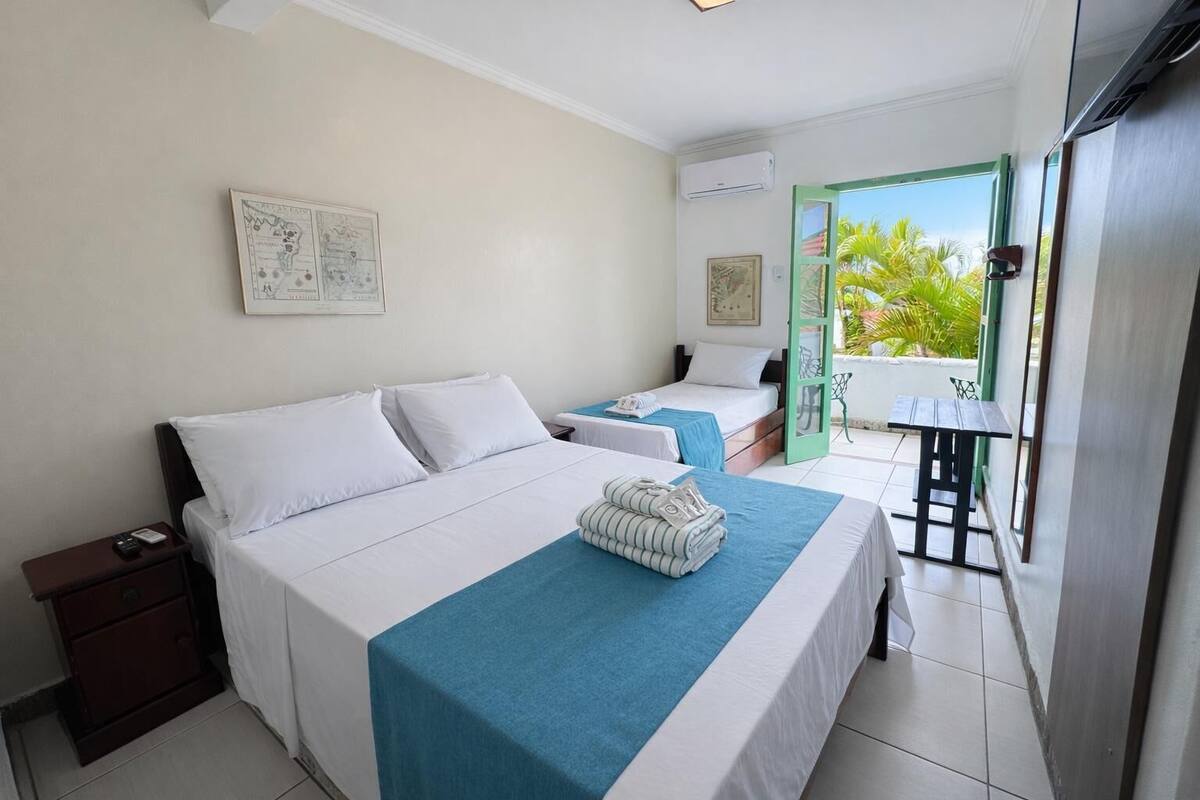A hotel room with two beds, a small table, and a balcony with a view.