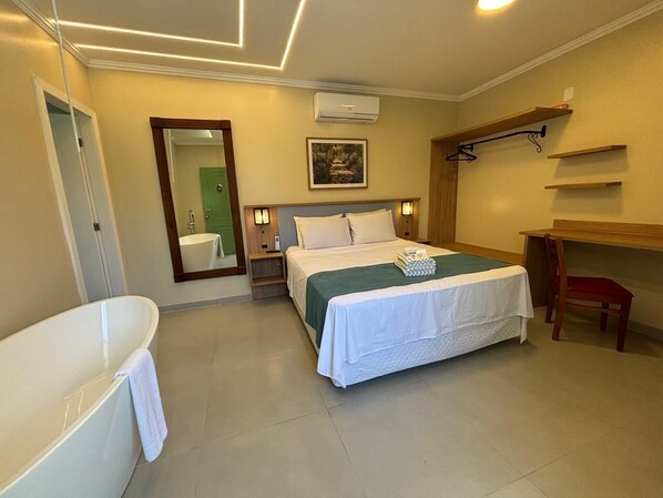 A hotel room with a large bed, a separate sitting area with a desk, a bathtub, and a mirror. - Estalagem do Porto (Arraial do Cabo)