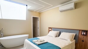 A modern bedroom with a large bed, a bathtub, and a ceiling air conditioner. - Estalagem do Porto (Arraial do Cabo)