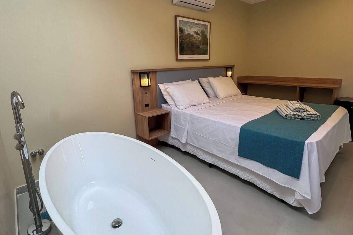 A modern hotel room with a large bathtub, a neatly made bed, and a wall-mounted air conditioner.