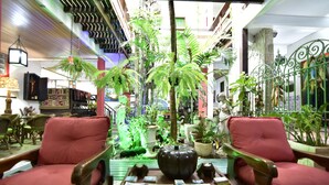 A cozy indoor space with wooden chairs, a central table with magazines, and various potted plants. - Estalagem do Porto (Arraial do Cabo)