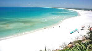 A beach with clear turquoise waters, white sand, and a few people. There are blue umbrellas and a lifeguard tower visible. - Estalagem do Porto (Arraial do Cabo)