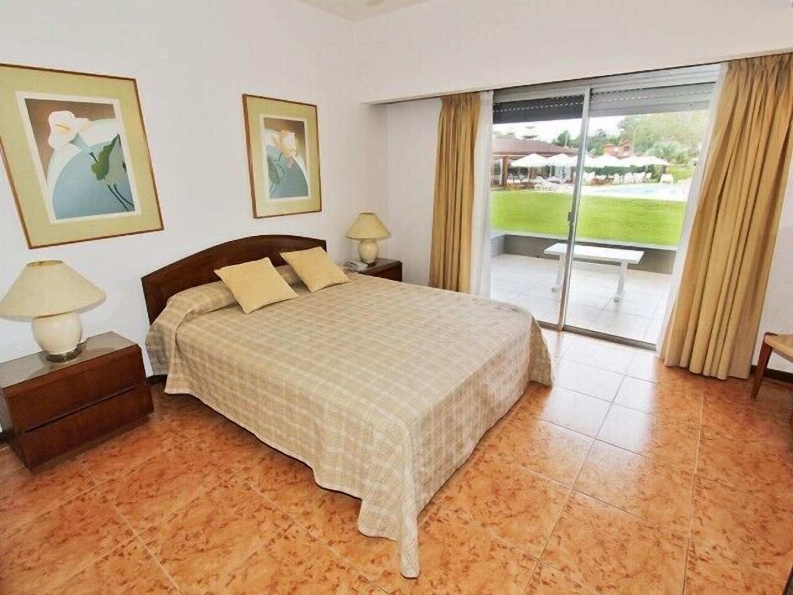 Un dormitorio con cama, mesitas de noche y vistas a un jardín a través de un ventanal corredero.