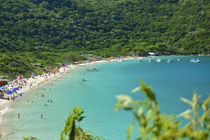 A beach with clear turquoise water, surrounded by lush green hills. - Hotel da Canoa (Arraial do Cabo)