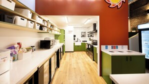 Une cuisine avec un plancher en bois, des comptoirs blancs, des armoires vertes et un néon.