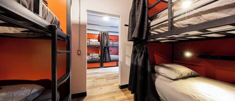 A dormitory room with bunk beds, a wooden floor, and a door leading to another room.