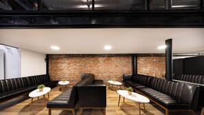 Un salon moderne avec des canapés en cuir et des tables rondes, un mur en briques et un plafond haut.