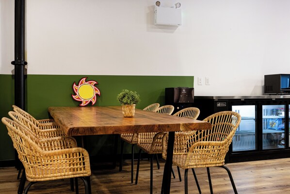 Un comedor con mesa de madera, sillas de mimbre, una planta en maceta y un aire acondicionado instalado en la pared.
