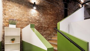 Un escalier aux panneaux verts et blancs, un mur de briques et une étagère blanche ornée de plantes.