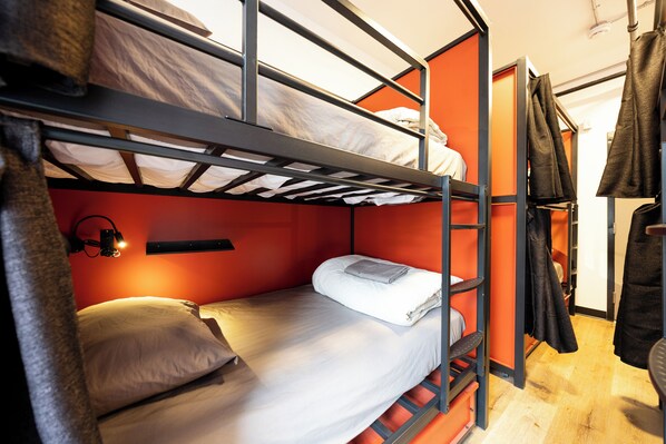 A bunk bed room with a red wall, a small shelf, and a hanging coat rack.