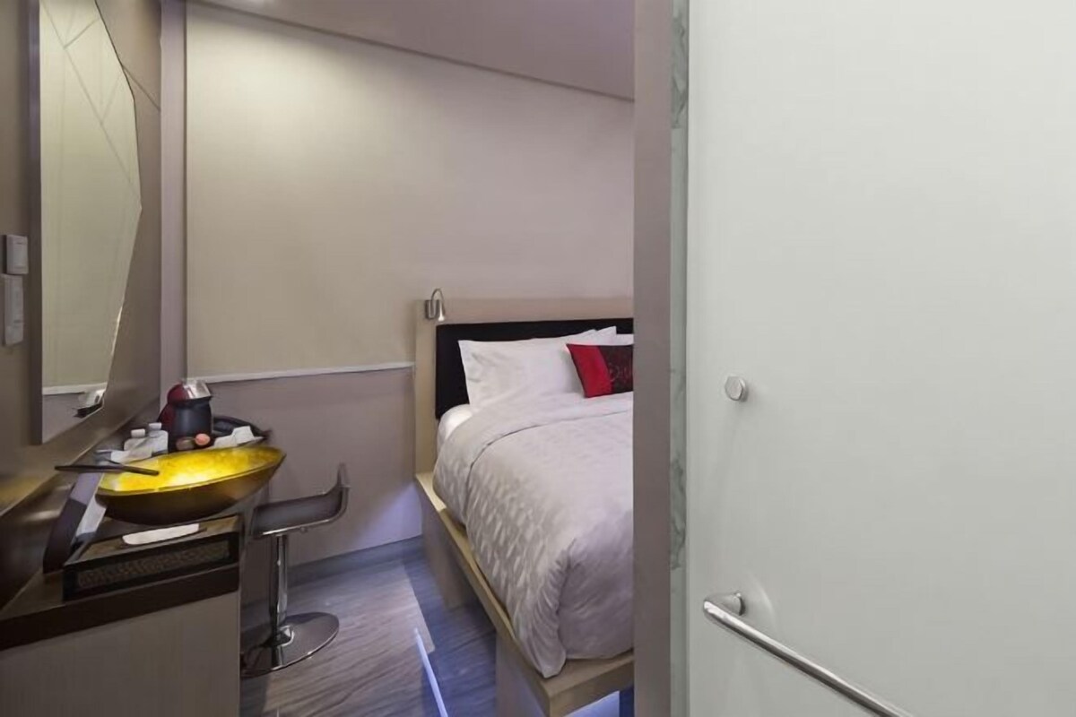A hotel room with a bed, a bedside table, a mirror, and a sink.