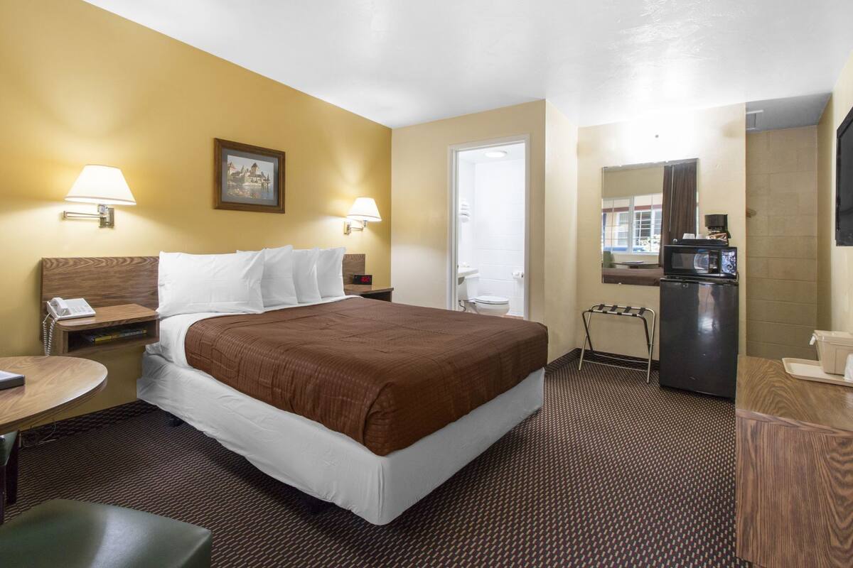 Hotelkamer met een bed, bedlampen, een bureau met telefoon, een klein tafeltje, een stoel, een koelkast en een magnetron.