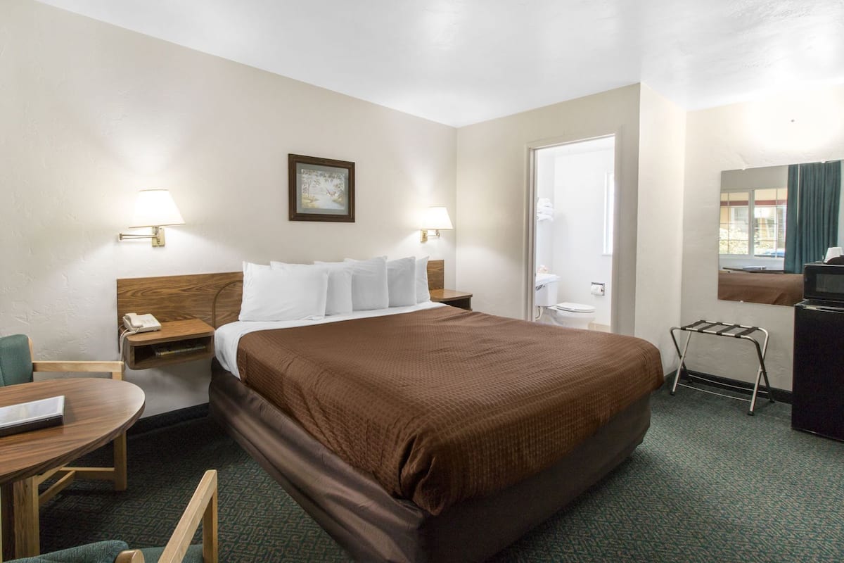 Een hotelkamer met een bed, nachtkastjes, een bureau, een stoel, een lamp, een schilderij aan de muur en een raam met gordijnen.