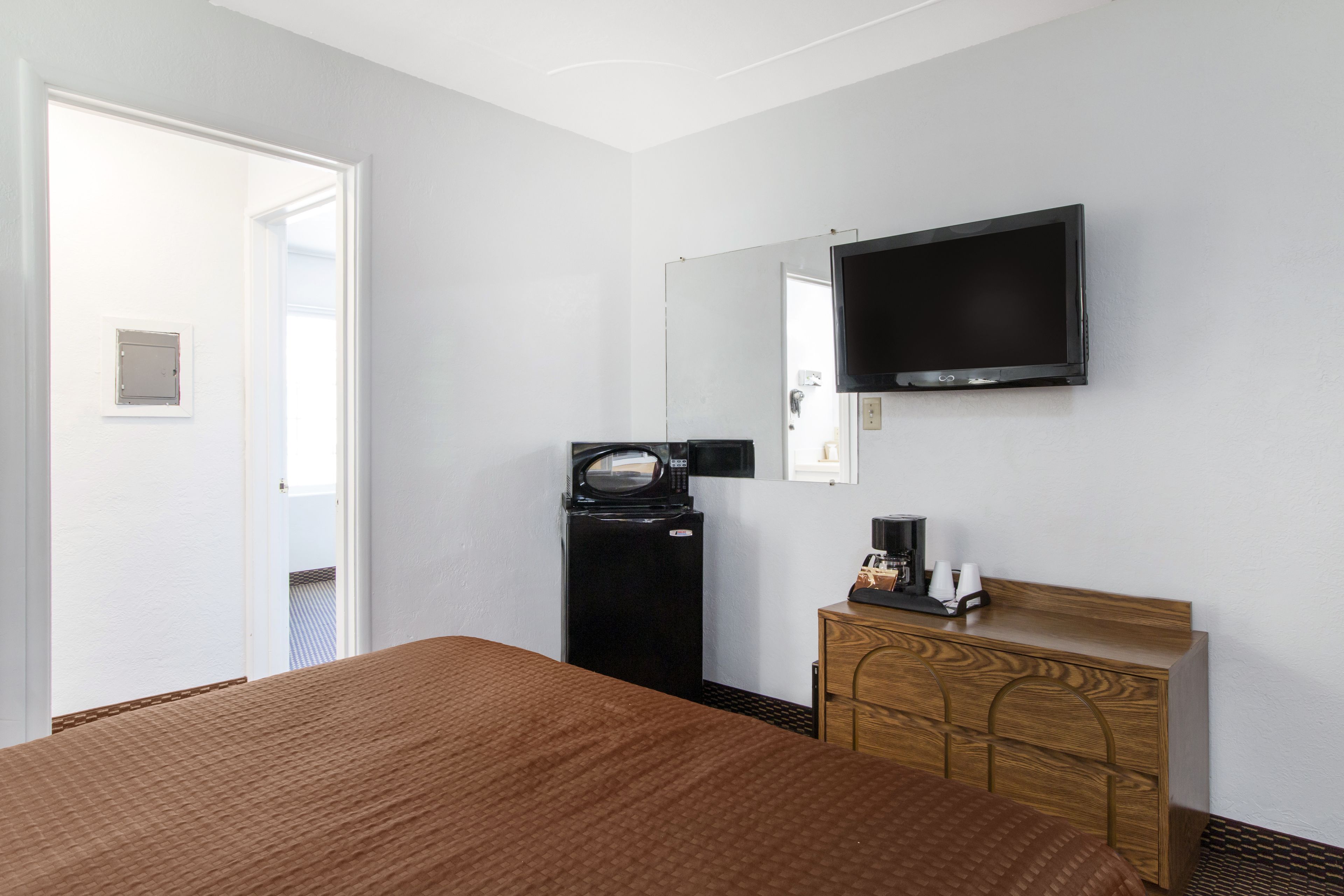 A hotel room with a bed, a wooden dresser, a television mounted on the wall, and a microwave on a small table.