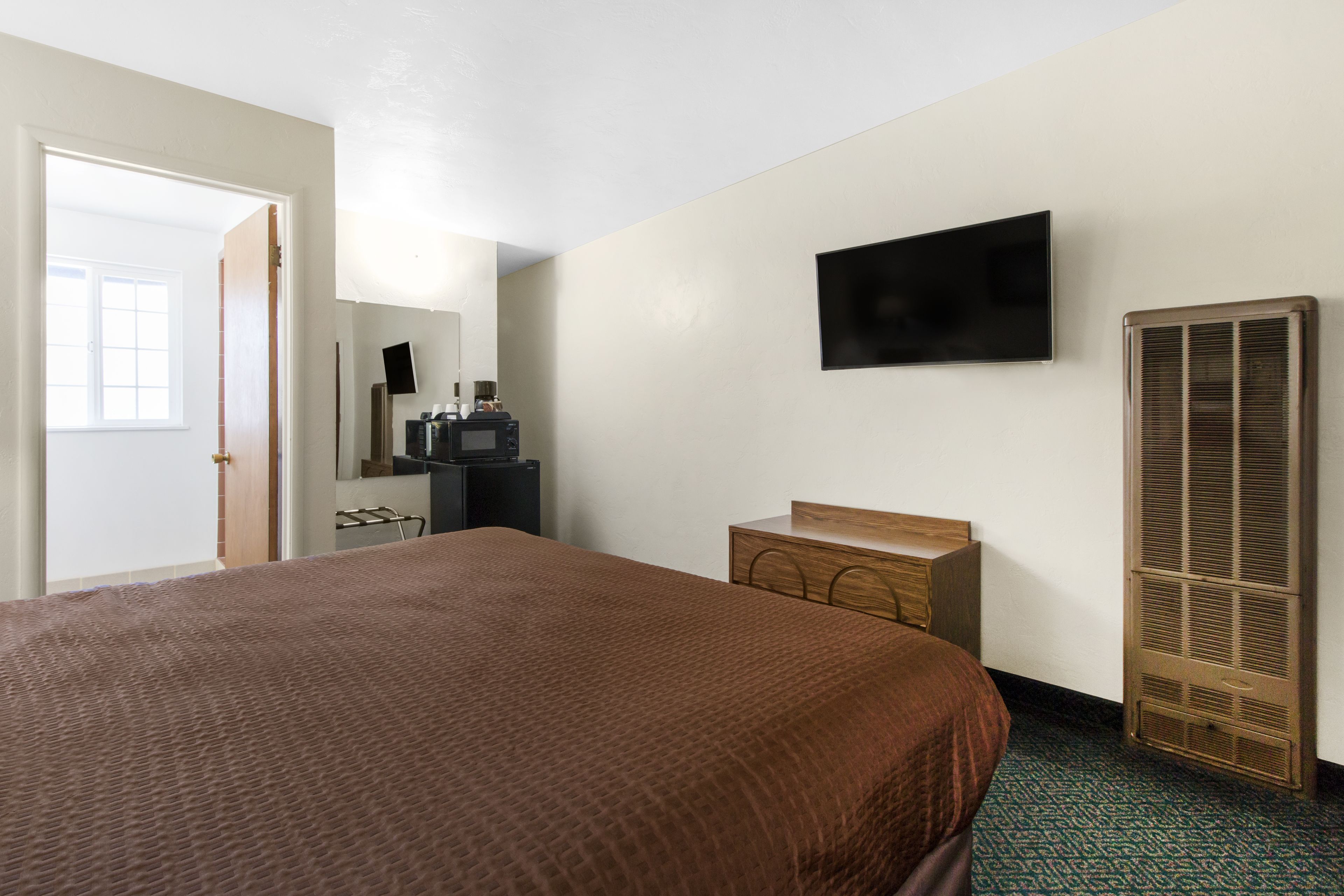 A hotel room with a large bed, a flat-screen TV mounted on the wall, a wooden dresser, a walk-in closet, and a window with a view.