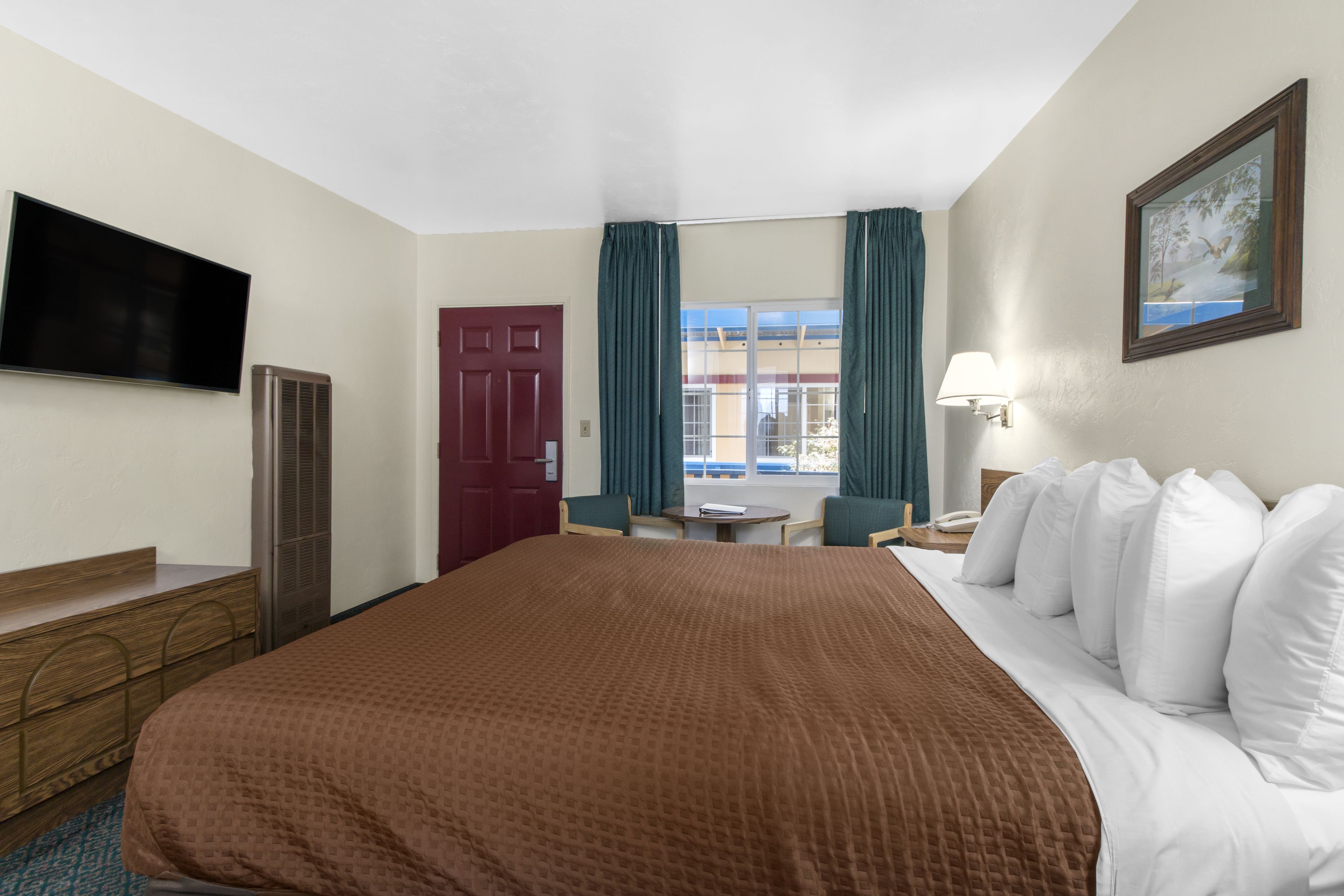 A hotel room with a large bed, a TV, a desk, and a window with curtains.