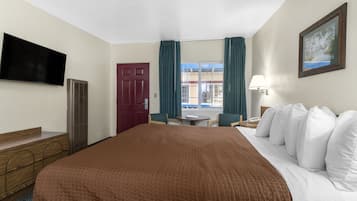 A hotel room with a large bed, a TV, a desk, and a window with curtains.