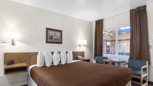 A hotel room with a large bed, two bedside lamps, a digital clock, a small table, a chair, and a window with curtains. - Town House Motel – Historic Old Town Eureka (Eureka)
