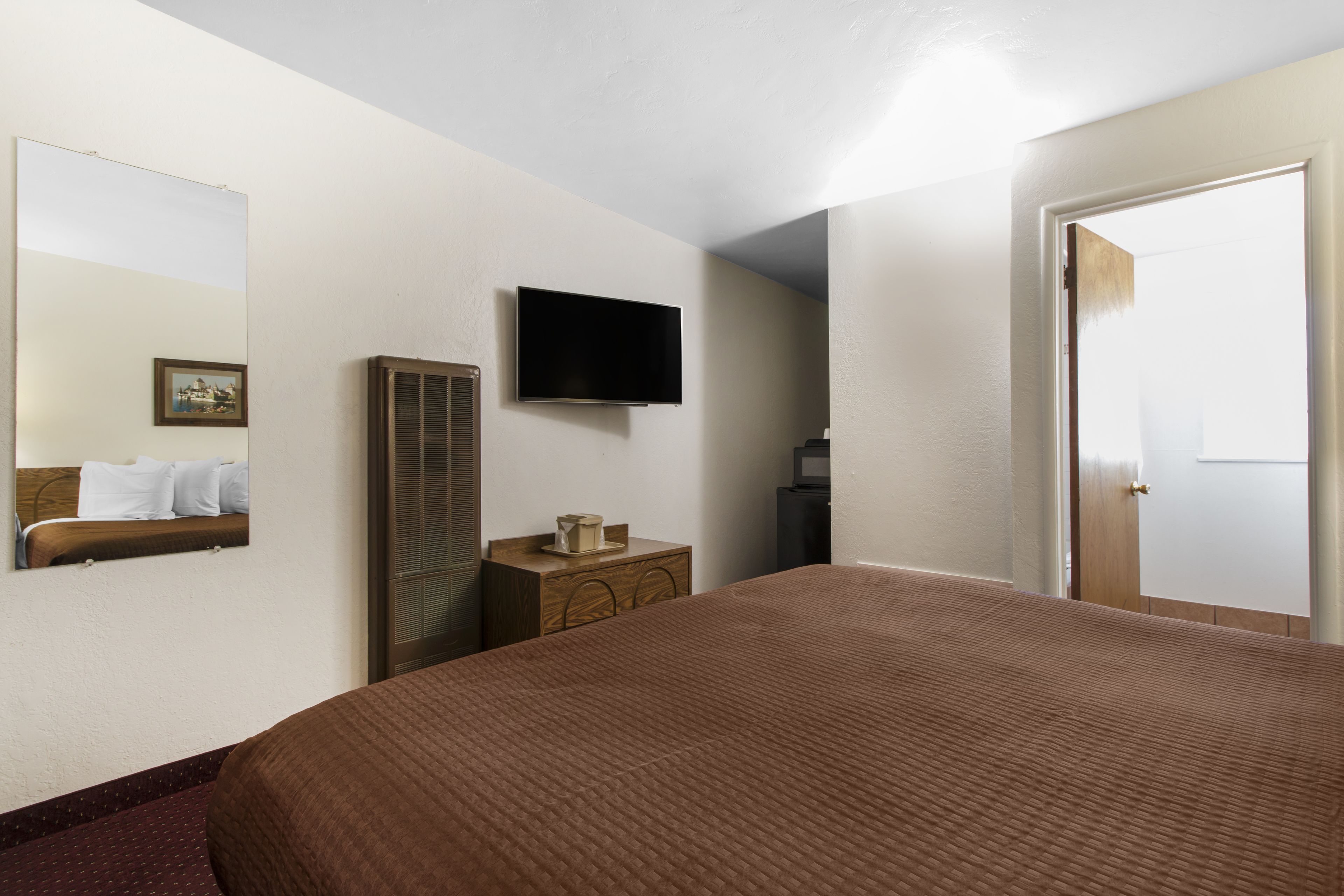 Habitación de hotel con una cama grande, un televisor de pantalla plana en la pared, un aparador y una puerta.