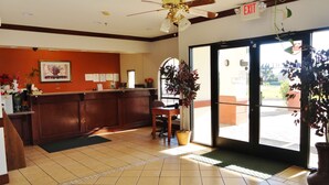 A reception area with a wooden reception desk, a ceiling fan, and a large potted plant near the entrance. - Americas Best Value Inn Brownsville (Brownsville)