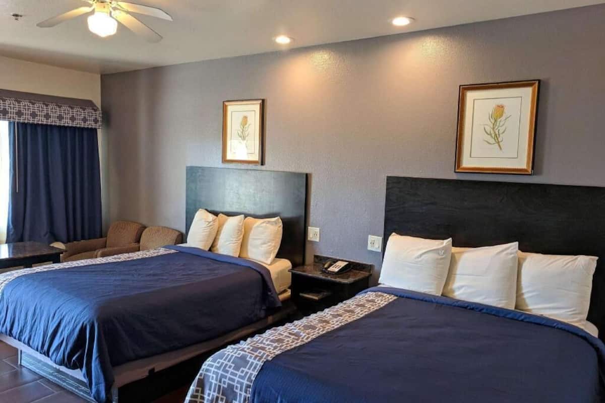 Une chambre d’hôtel avec deux lits, un ventilateur de plafond, des œuvres d’art encadrées accrochées aux murs et une table de chevet avec un téléphone.