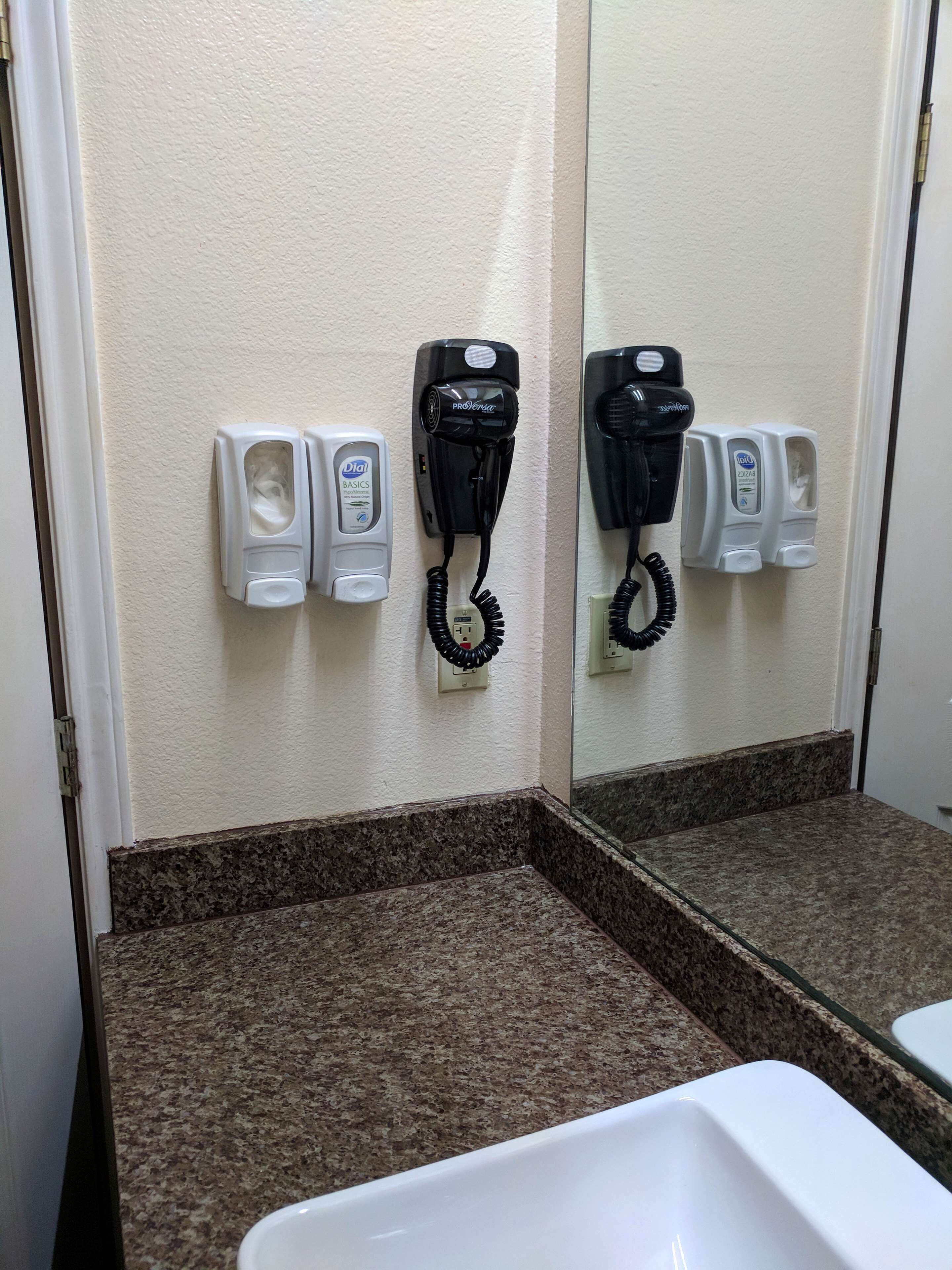 Un baño con encimera de mármol, un lavamanos, un espejo y dos secadores de pelo fijados en la pared.