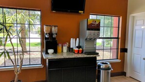 A coffee station with a Folgers coffee machine, a trash can, and a potted plant. - Americas Best Value Inn Brownsville (Brownsville)