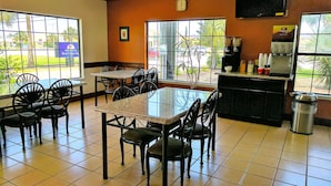 A restaurant with a glass-top table, black chairs, a coffee machine, and a trash can. - Americas Best Value Inn Brownsville (Brownsville)
