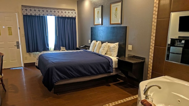A hotel room with a large bed, a bedside table, a nightstand, a bathroom with a bathtub, and a window with curtains. - Americas Best Value Inn Brownsville (Brownsville)