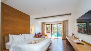 Habitación de hotel moderna con una cama grande, cabecera de madera, escritorio con silla y un amplio ventanal que ofrece vista a una piscina y follaje.