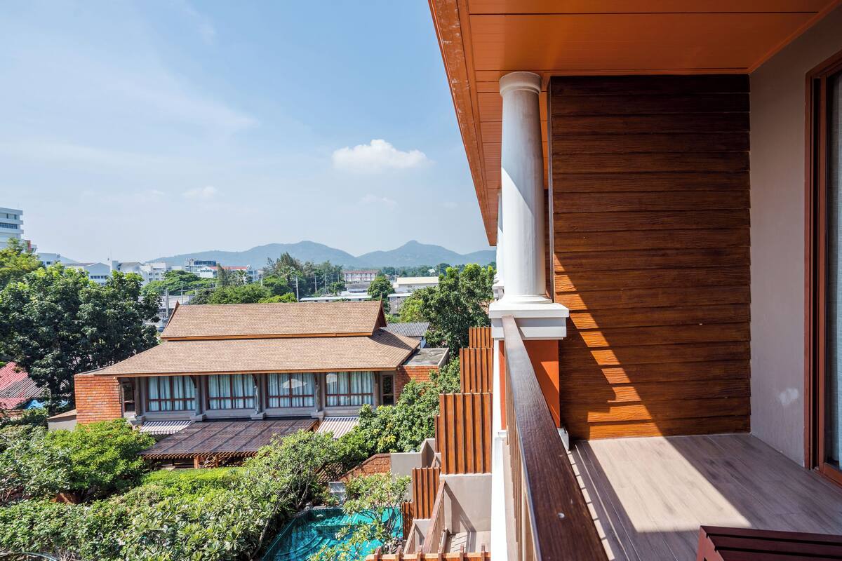 A modern building with a wooden facade, a balcony, and a view of surrounding buildings and mountains.