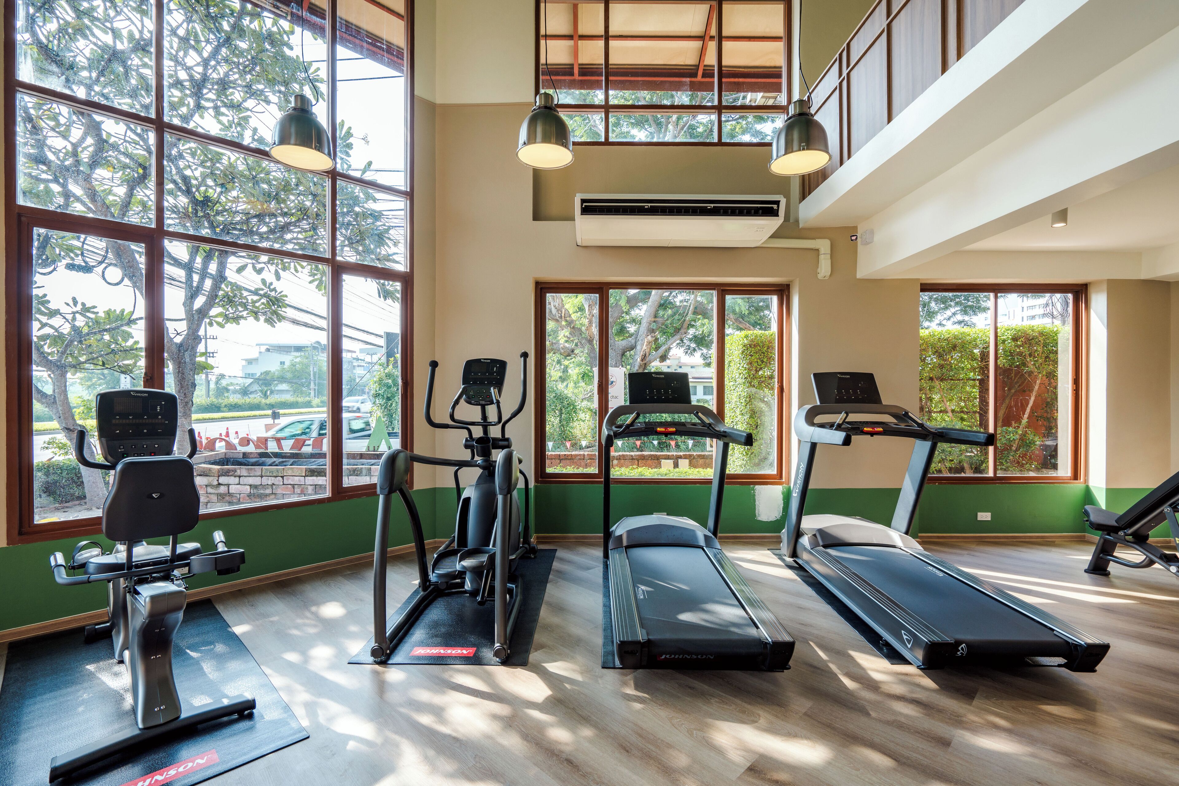 A gym with treadmills, elliptical machines, and a rowing machine. Large windows provide natural light and views of the outdoors.