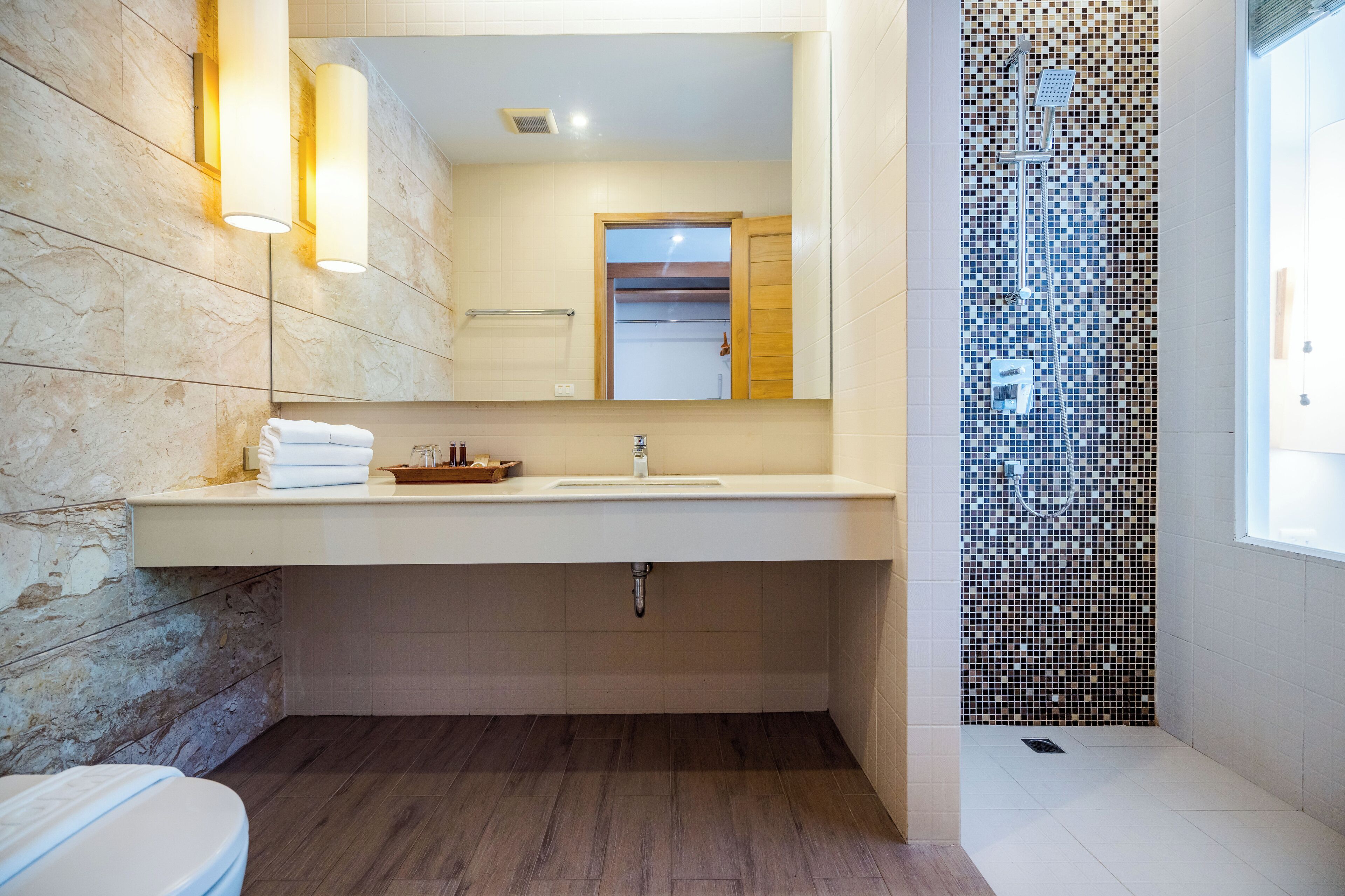 Un baño moderno con pared de piedra, un espejo grande, un lavamanos y una zona de ducha con mosaicos.