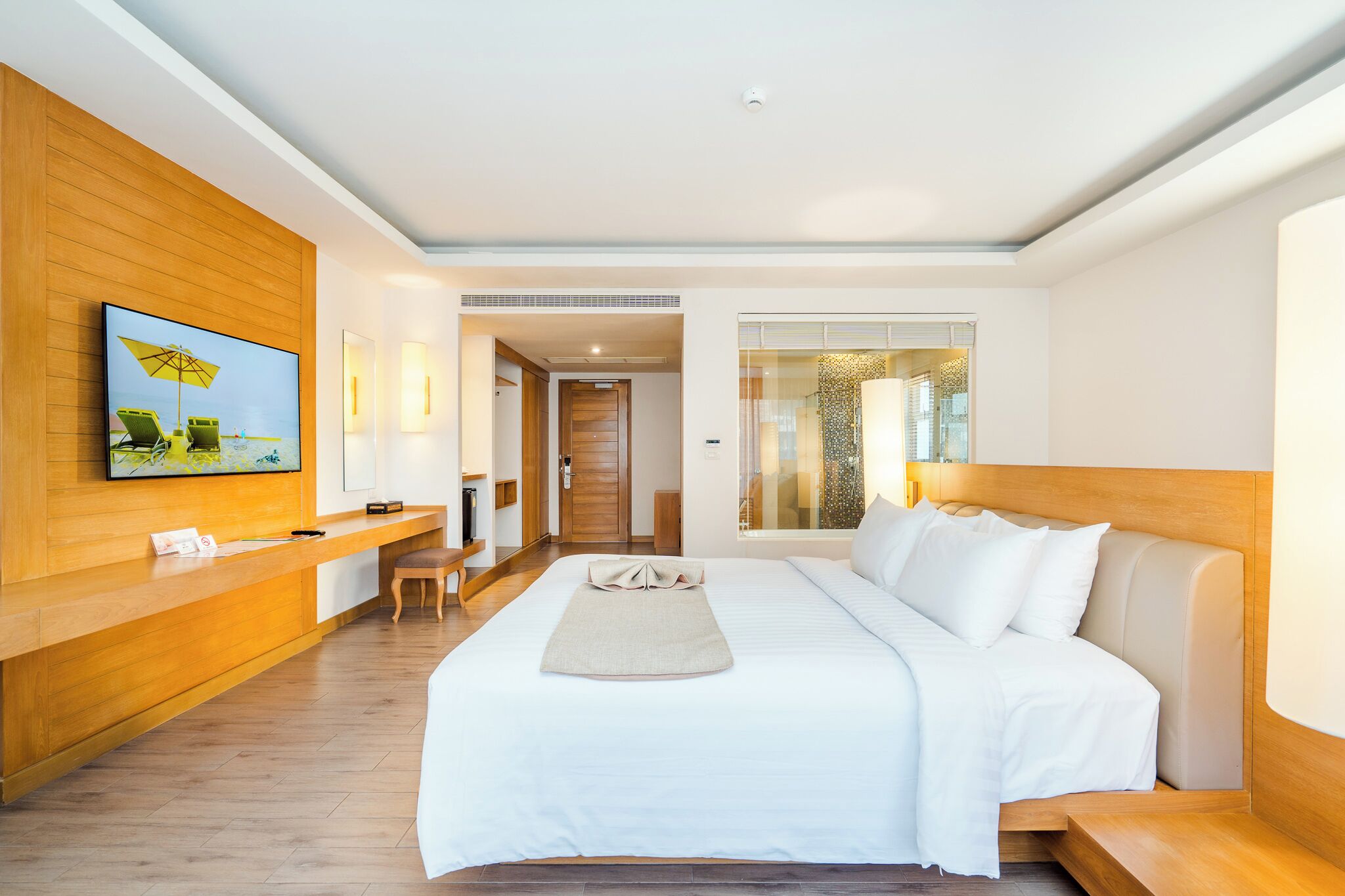 A hotel room with a large bed, a wooden reception desk, a TV, and a view of the outside.