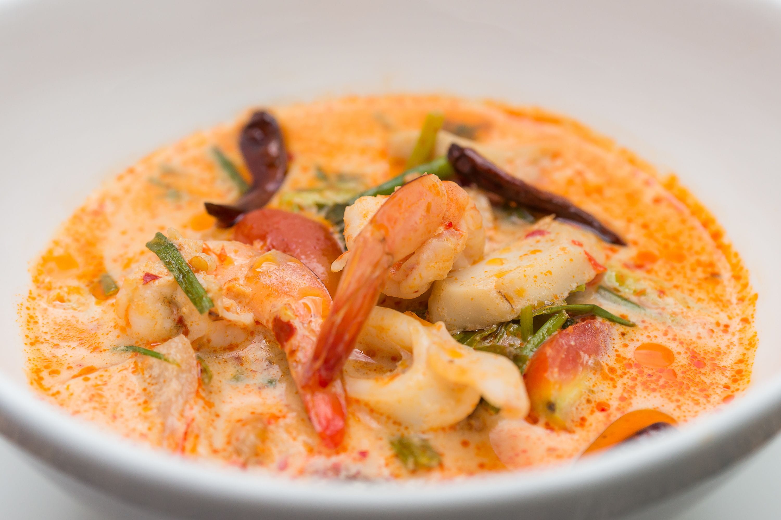 A bowl of seafood soup with shrimp, squid, and vegetables in a creamy broth.