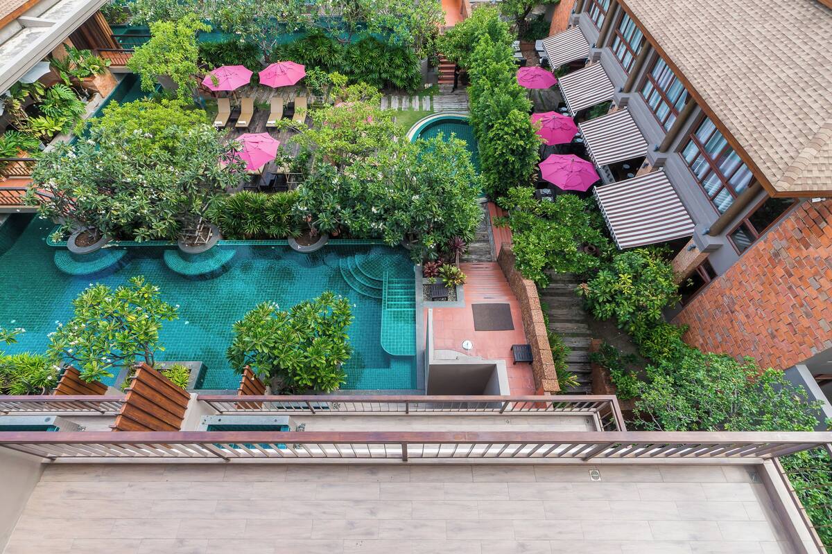 A rooftop pool area with multiple seating areas, surrounded by lush greenery and umbrellas.