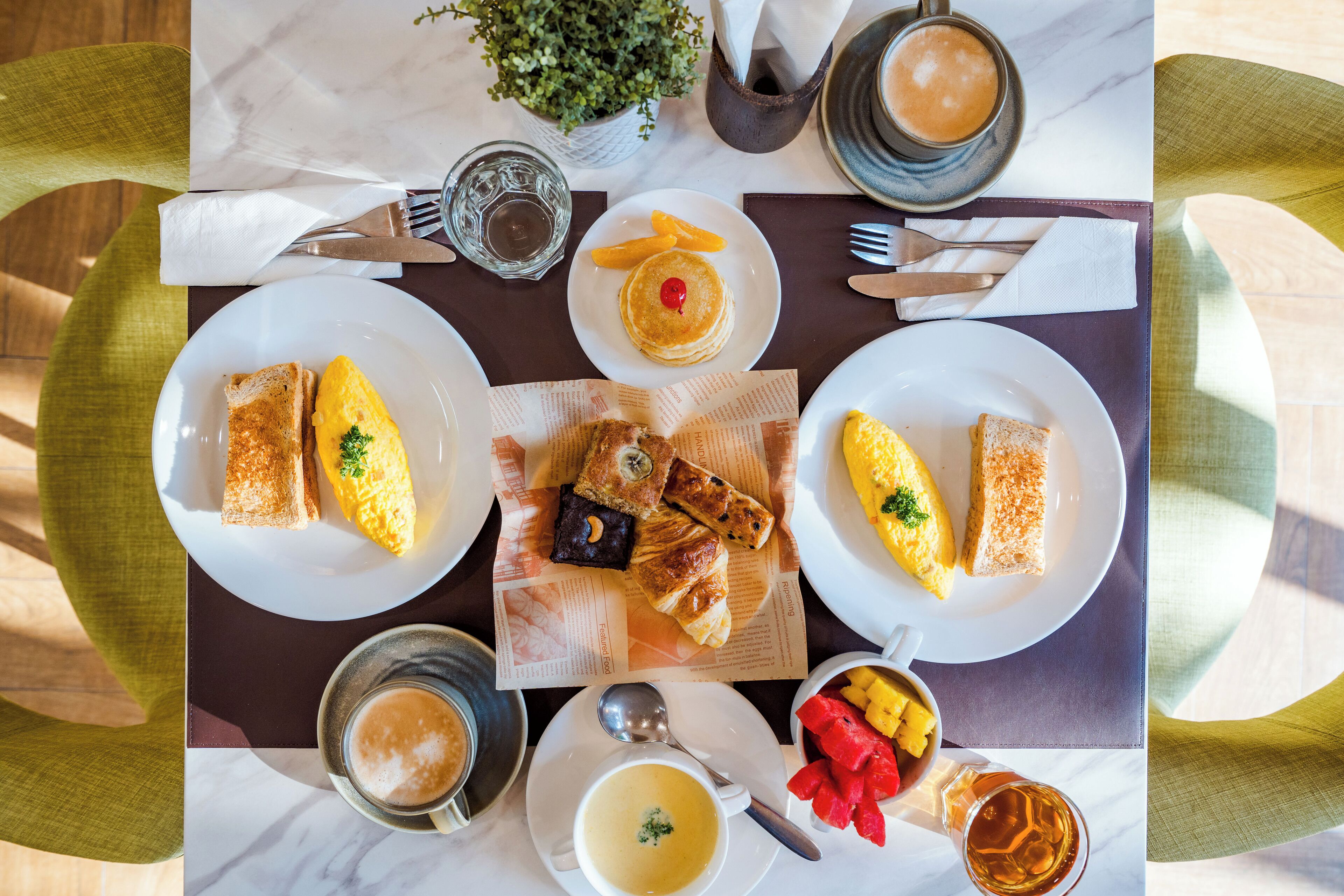 A breakfast setting with plates of toast, eggs, croissants, and fruit.