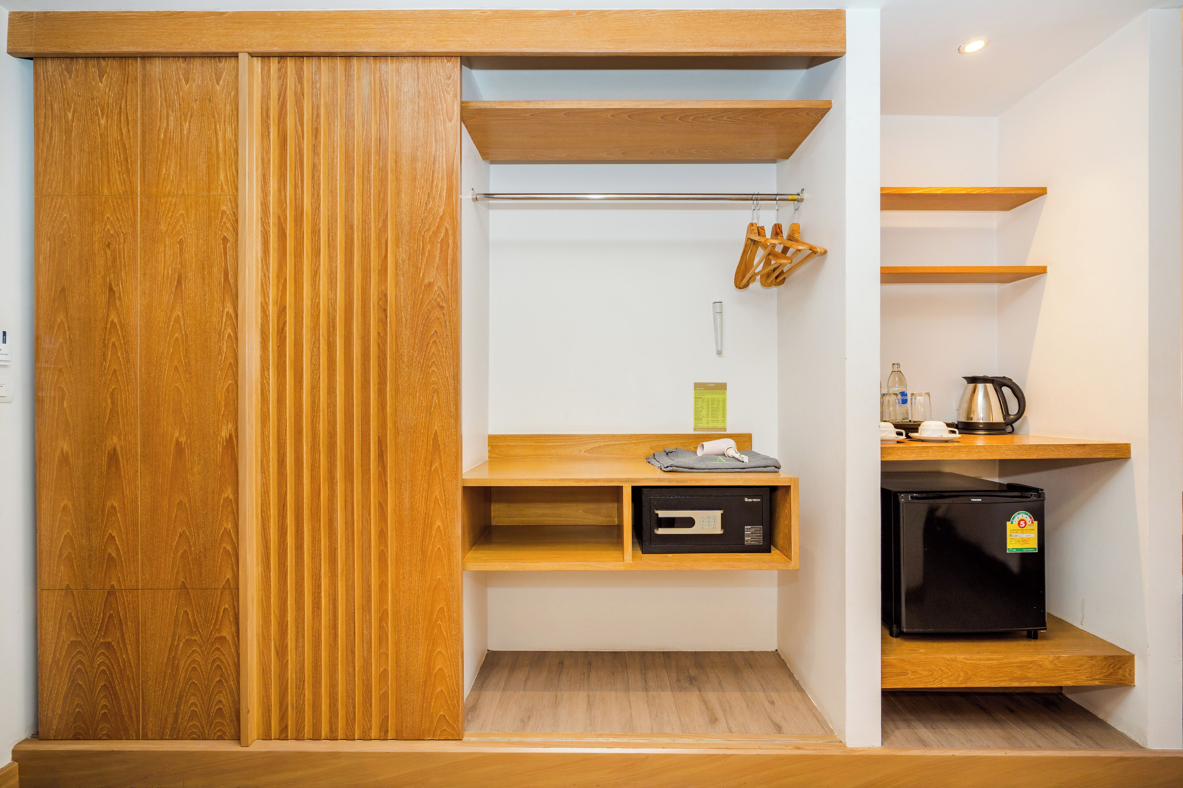 Een kleine keuken met houten planken, een zwarte koelkast en een hangende wasrek.