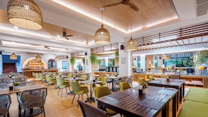Un restaurante espacioso con mesas y sillas de madera, lámparas de mimbre colgantes y una zona de bar.