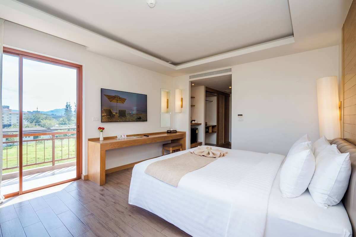 A modern hotel room with a large bed, a wooden desk, a balcony, and a city view.
