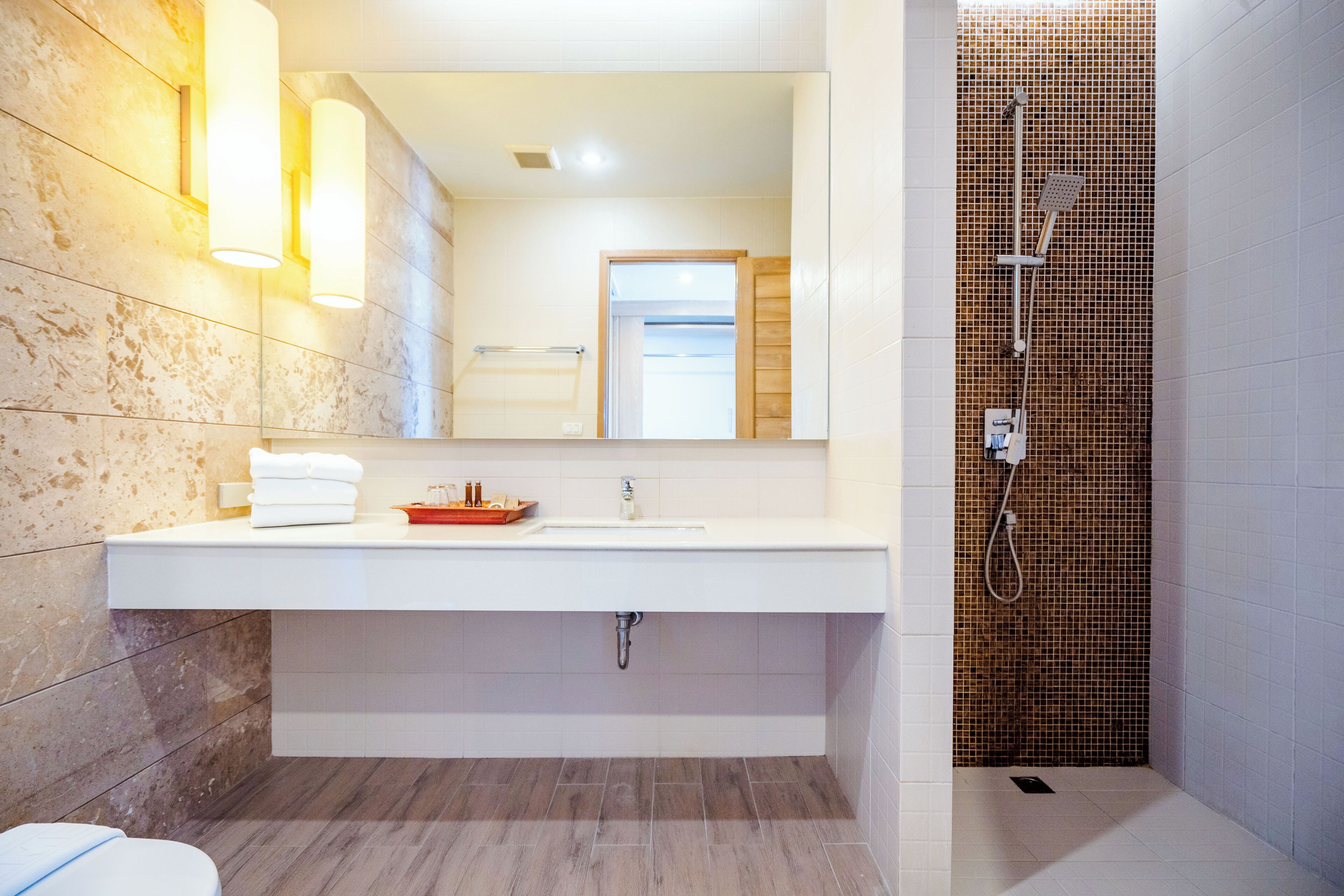 Un baño moderno con un espejo grande, lavamanos blanco y zona de ducha con mosaicos.