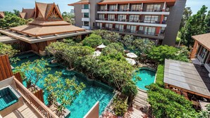 Un hotel con una gran piscina rodeada de abundante vegetación, varios balcones y un diseño arquitectónico moderno.