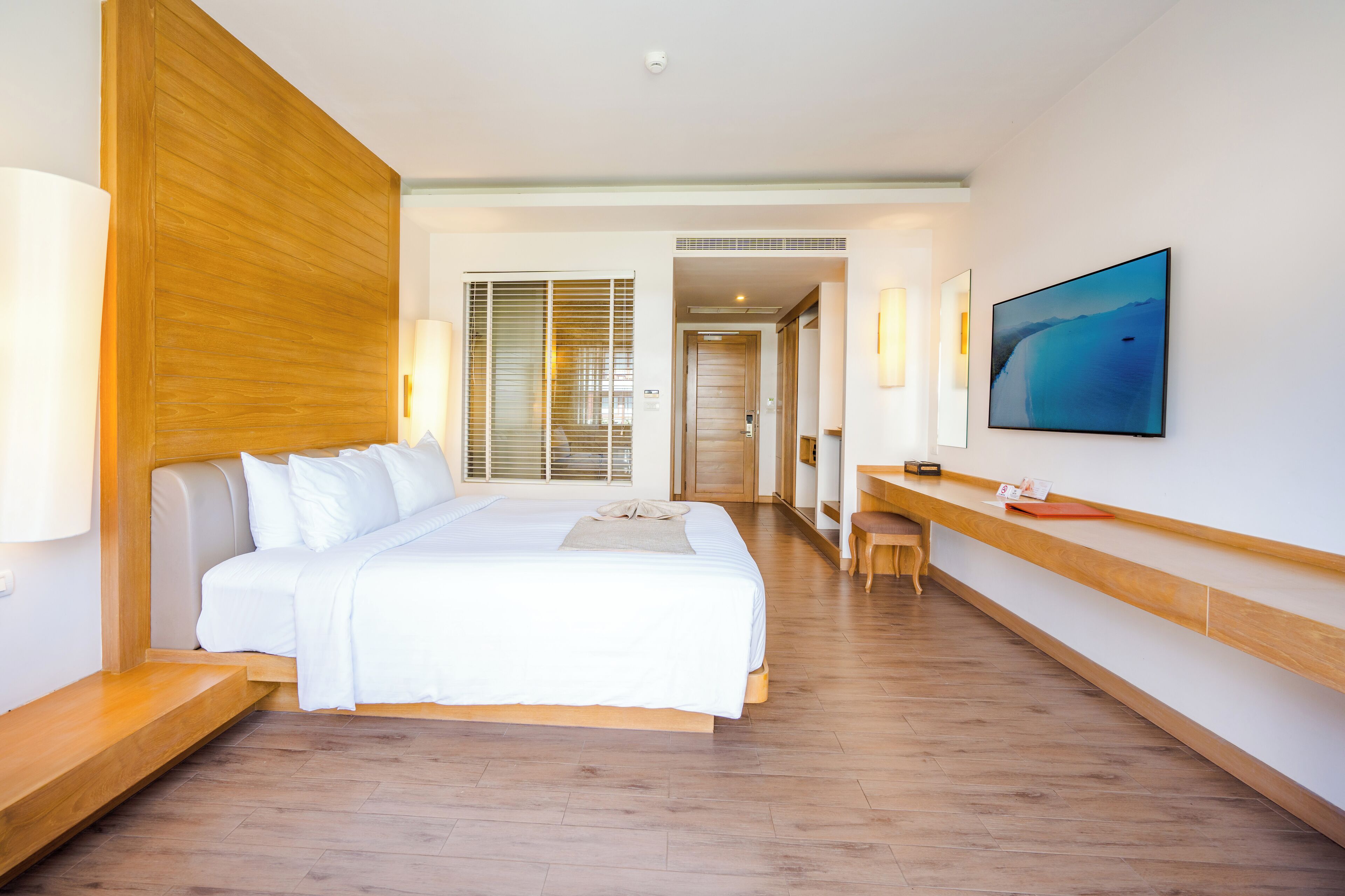 A hotel room with a large bed, a desk, and a TV on the wall.