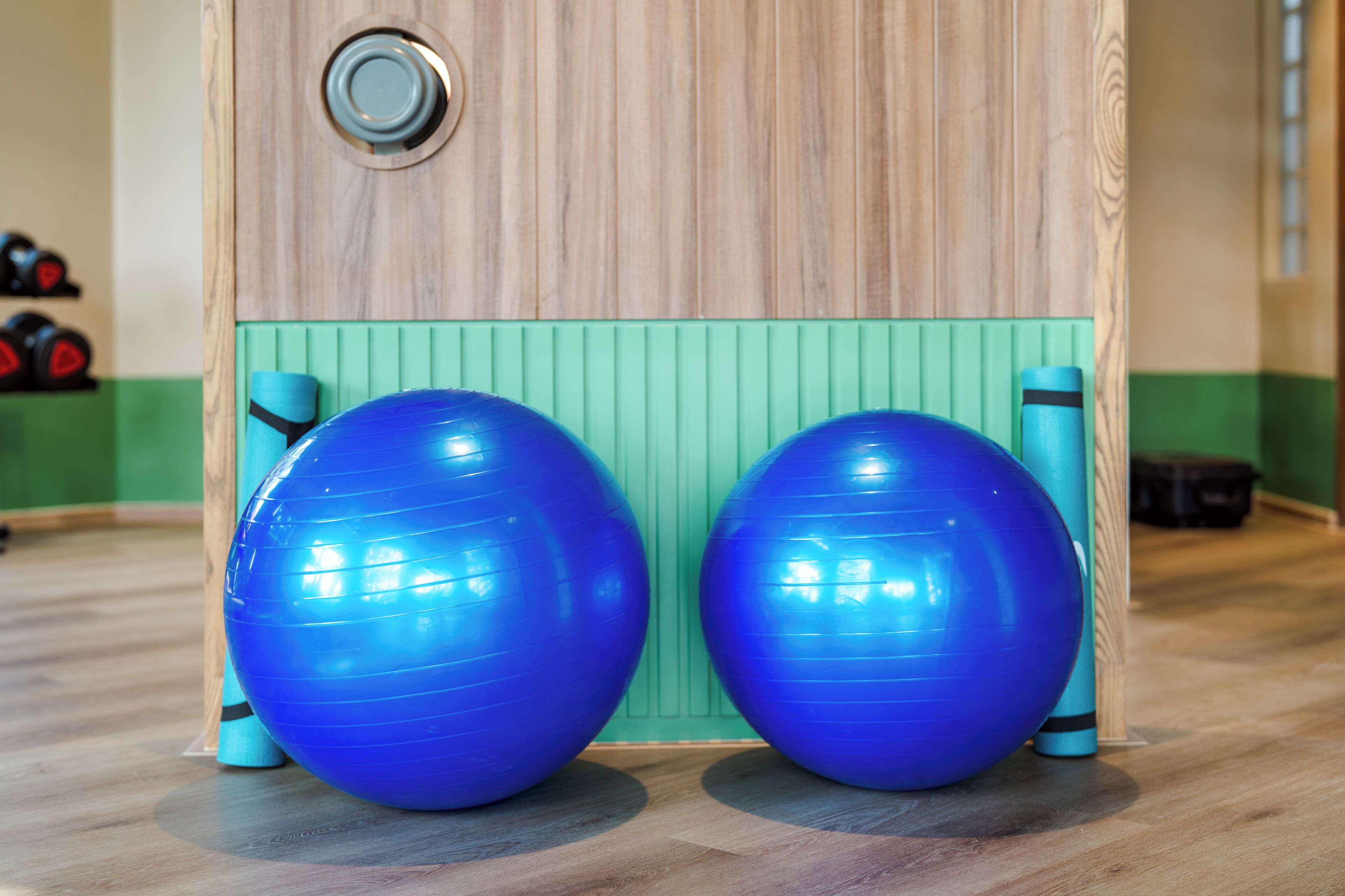 Two large blue exercise balls placed on a wooden floor with a green wall in the background.