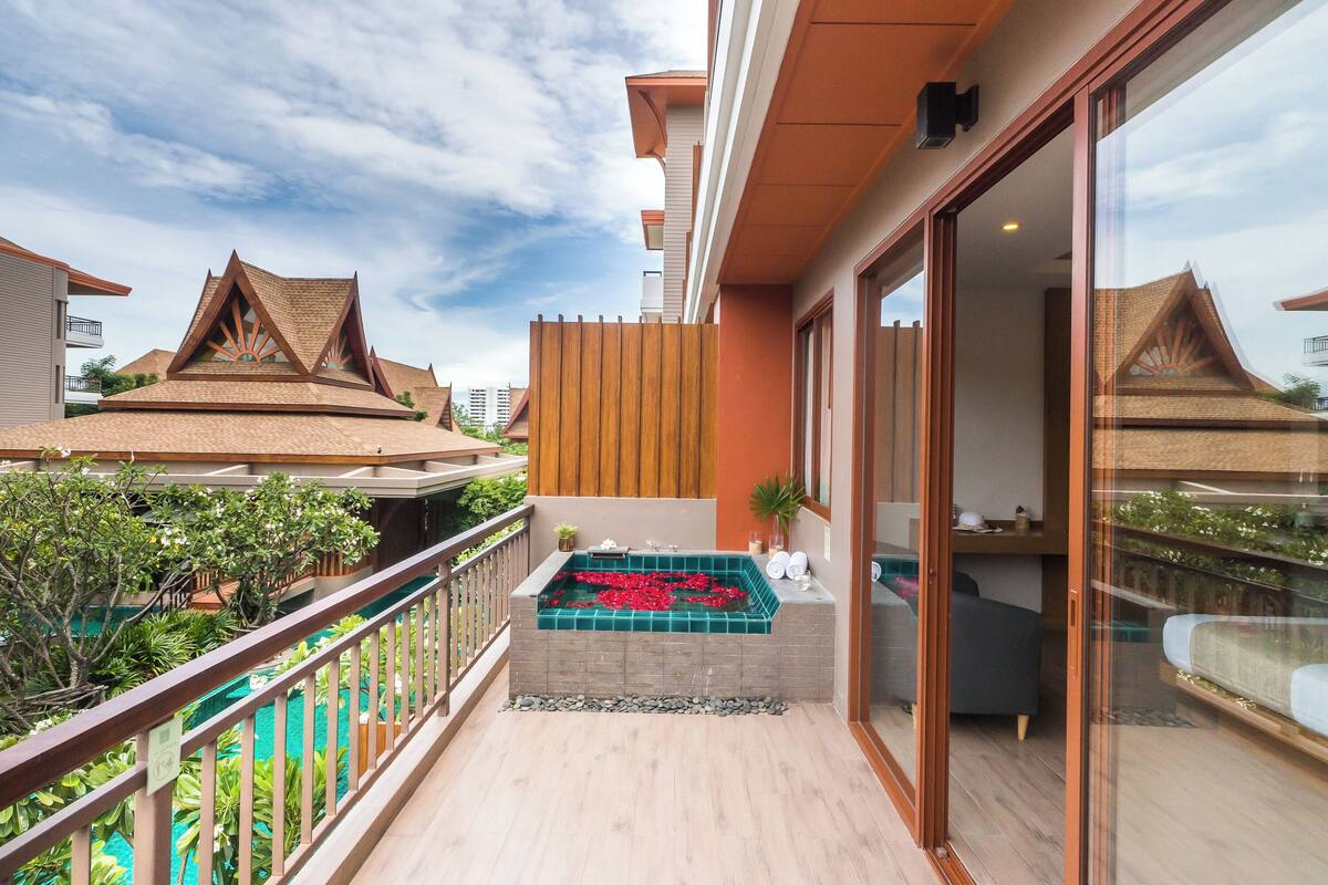 A balcony with a spa area, a wooden fence, and a view of neighboring buildings.