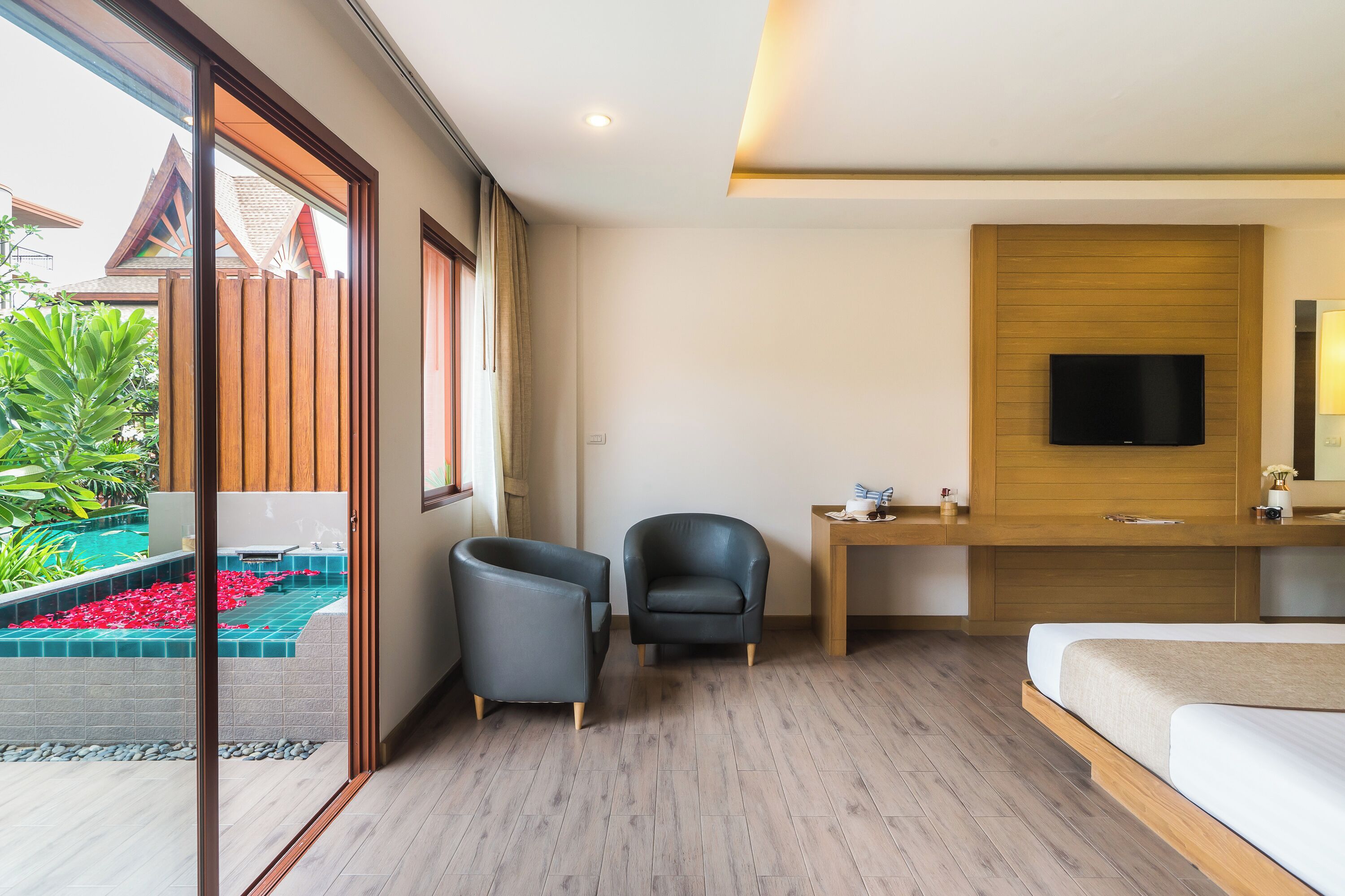 A modern hotel room with a bed, a desk, a chair, a TV, and a view of a swimming pool.