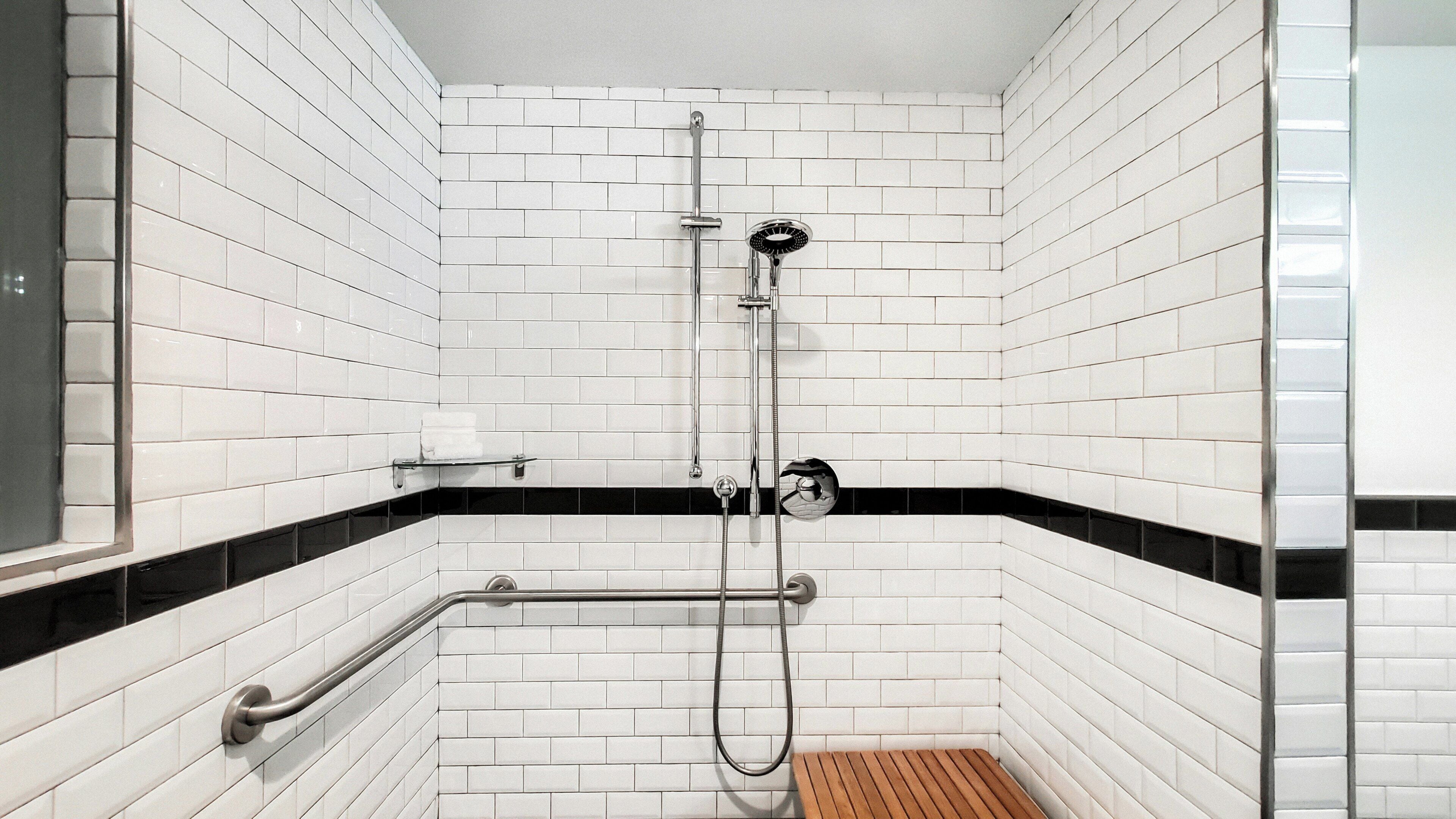 Una ducha con paredes de azulejos blancos, suelo de baldosas blanco y negro, y un banco de madera.