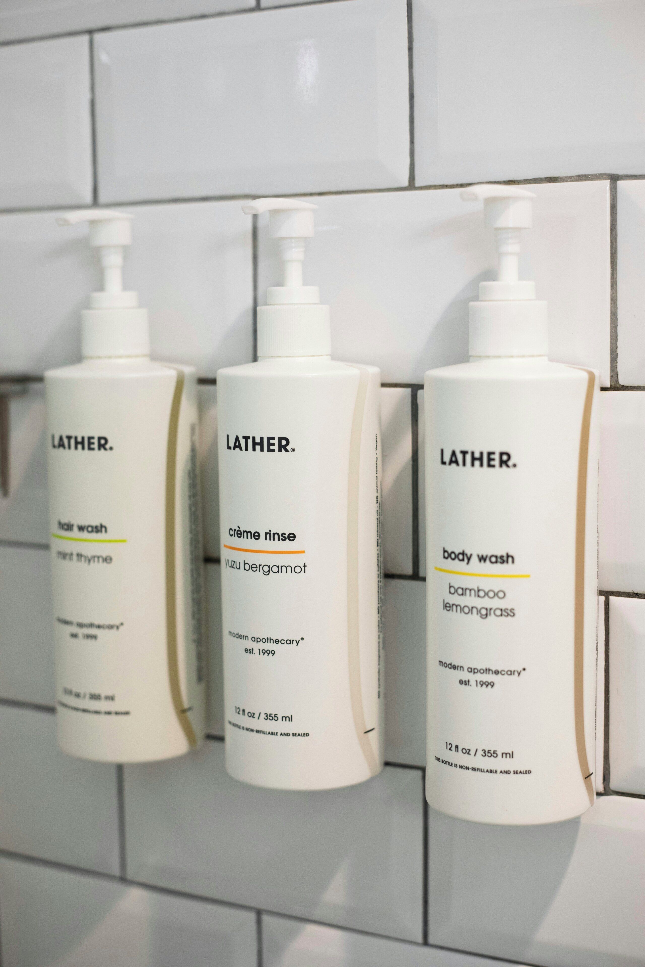 Tre flaskor med Lather-tvål på en vägg täckt med kakel.