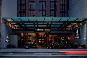 Entrada del Archer Hotel con un toldo de vidrio, fachada de ladrillo y el número 45 visible.