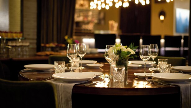 A restaurant table set with plates, glasses, and cutlery, with a decorative vase of flowers in the center. - Archer Hotel New York (New York)